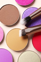 Different beautiful eye shadows and makeup brushes on beige background, flat lay