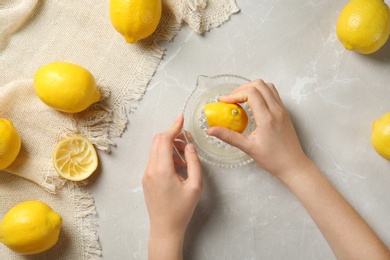 Photo of Young woman squeezing lemon with juicer on light table