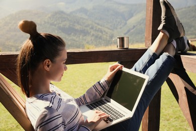 Photo of Young woman working with laptop on outdoor wooden terrace in mountains