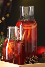 Photo of Glass bottles of aromatic punch drink and Christmas decor on dark background, closeup