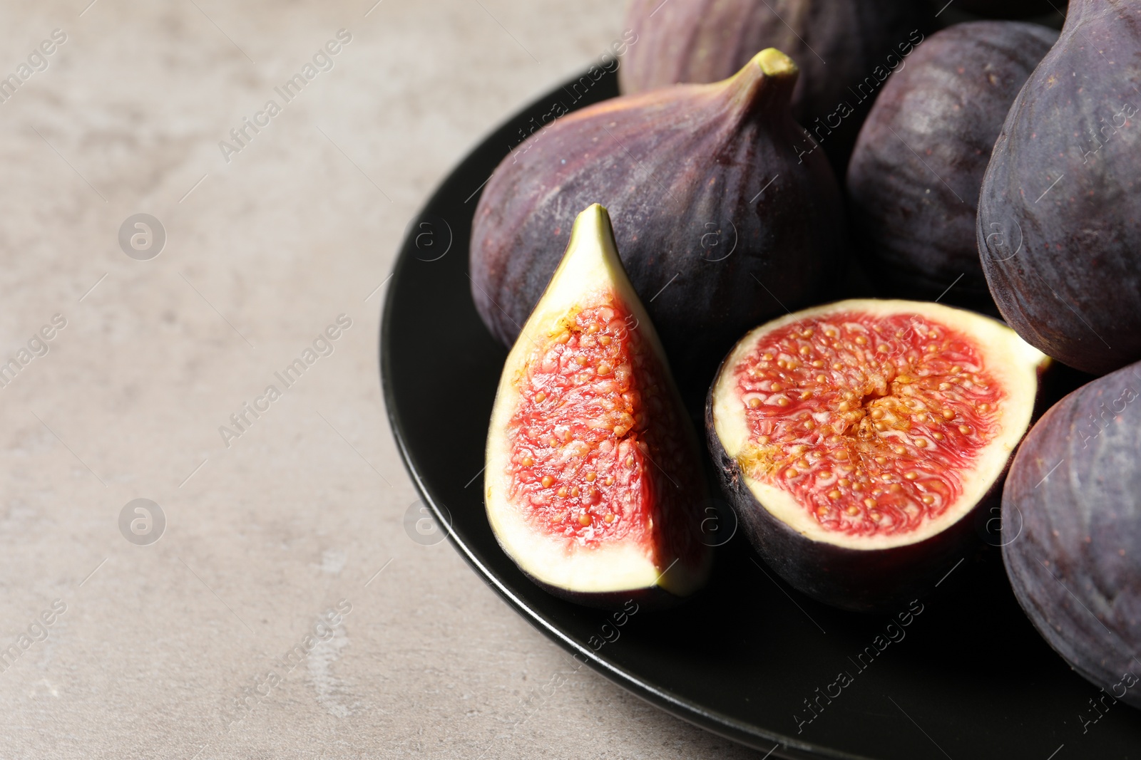 Photo of Whole and cut ripe figs on light grey textured table, closeup. Space for text