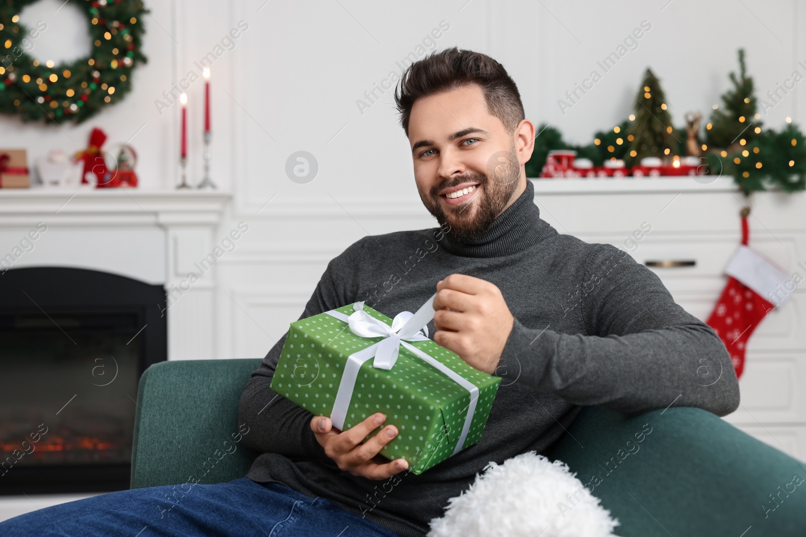 Photo of Happy young man opening Christmas gift at home