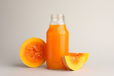 Tasty pumpkin juice in glass bottle and cut pumpkin on light background