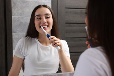 Young woman brushing her teeth with electric toothbrush near mirror in bathroom