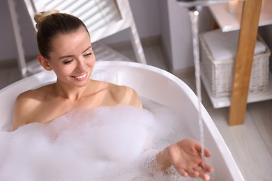 Beautiful woman taking bath in tub with foam indoors. Space for text
