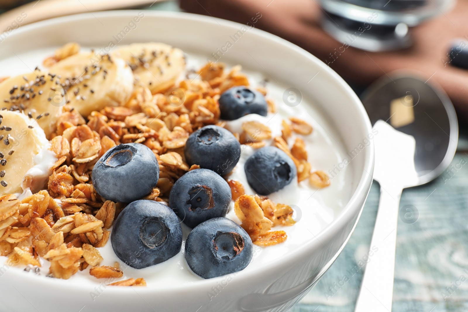 Photo of Bowl of yogurt with blueberries, banana and oatmeal on wooden table, closeup
