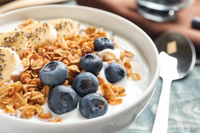 Bowl of yogurt with blueberries, banana and oatmeal on wooden table, closeup