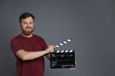 Making movie. Smiling man with clapperboard on grey background. Space for text