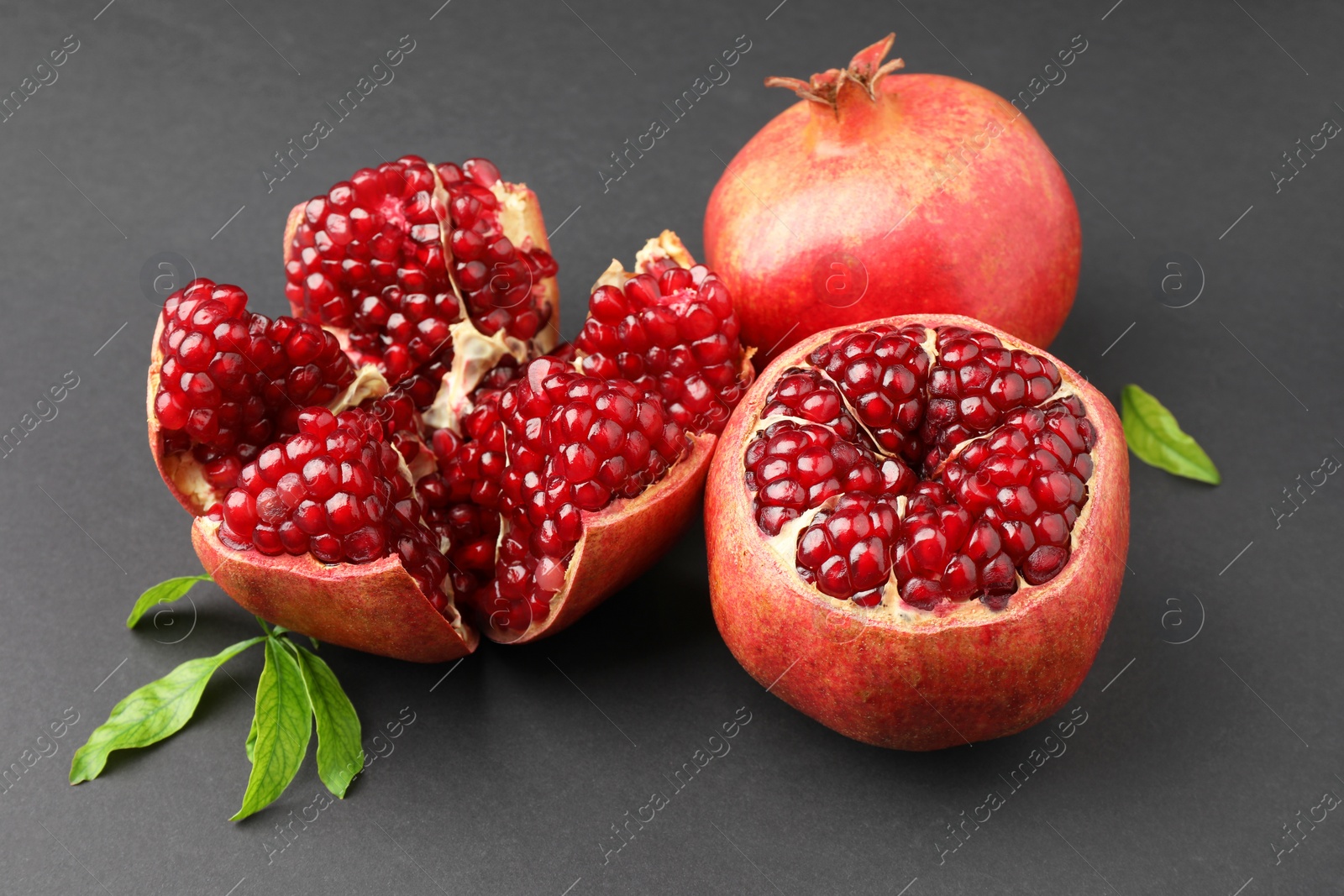 Photo of Fresh ripe pomegranates and leaves on grey background