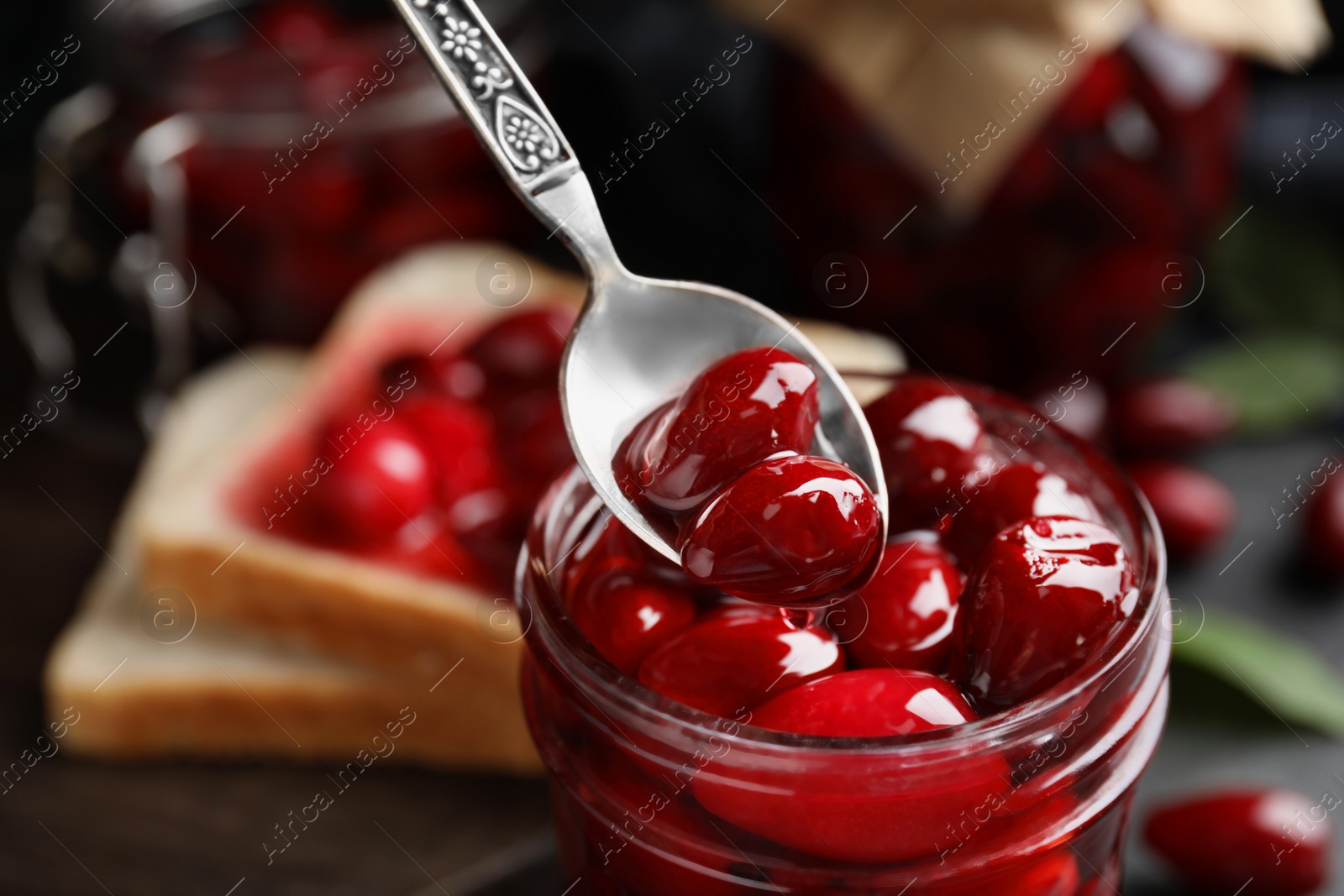 Photo of Delicious dogwood jam with berries in glass jar and spoon, closeup. Space for text