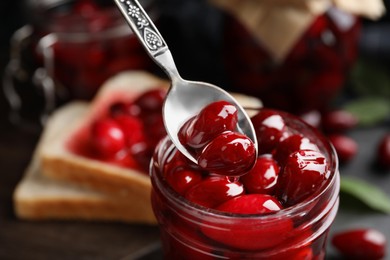 Delicious dogwood jam with berries in glass jar and spoon, closeup. Space for text