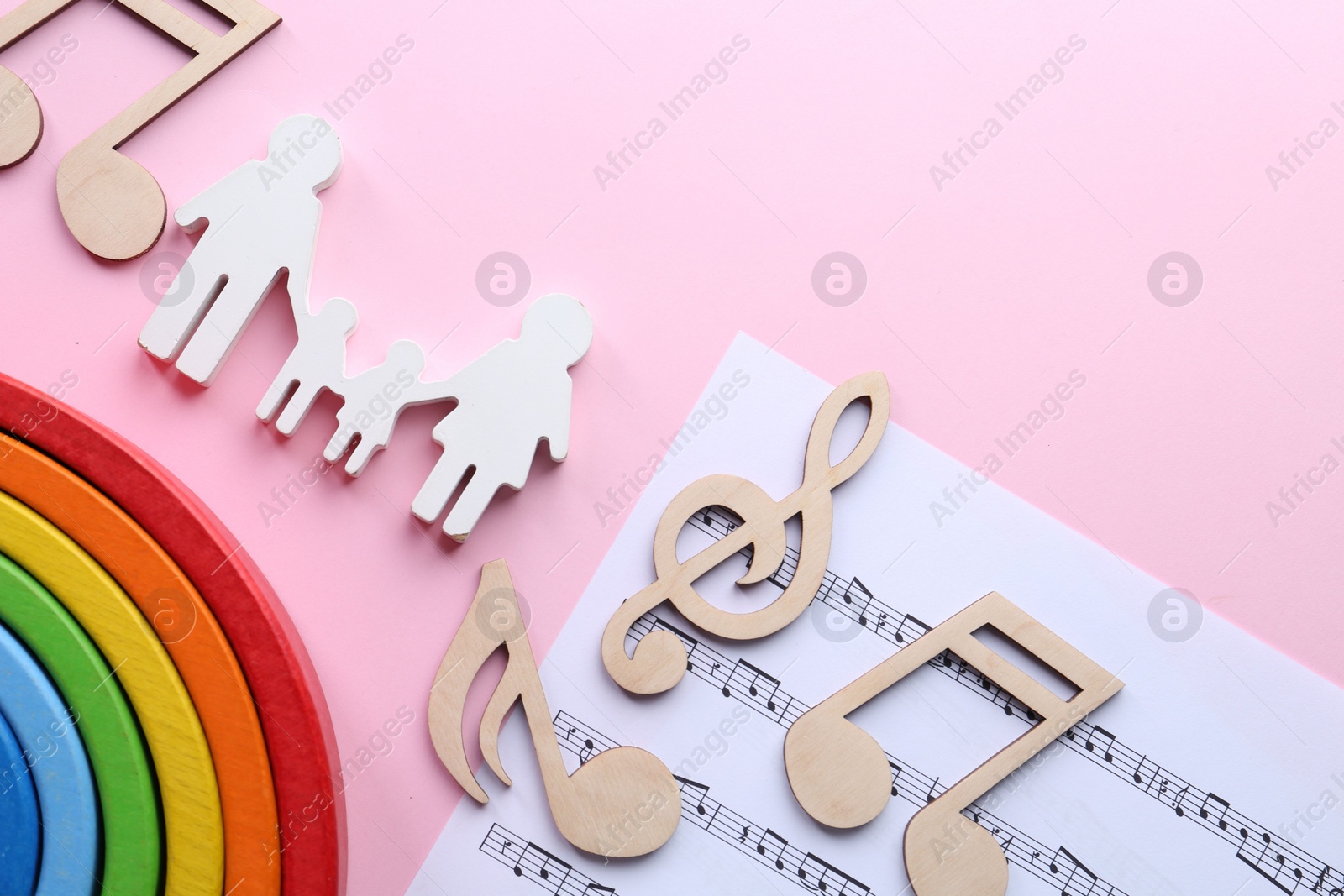 Photo of Baby songs. Music sheet, figures of family, wooden notes and toy rainbow on pink background, flat lay