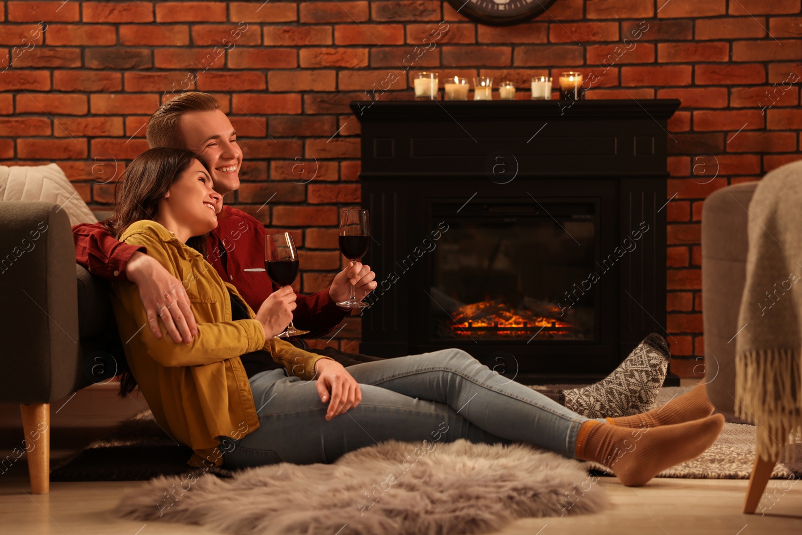 Photo of Happy lovely couple with glasses of wine resting together on floor near fireplace at home
