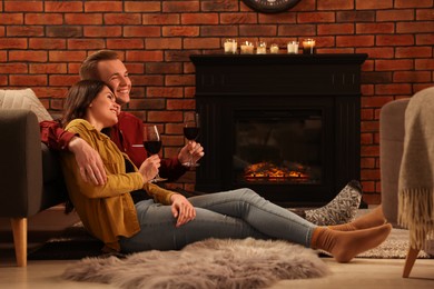 Happy lovely couple with glasses of wine resting together on floor near fireplace at home