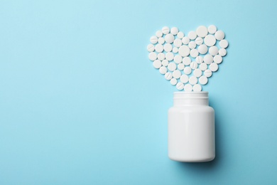 Photo of Heart made of pills and container on color background, top view with space for text