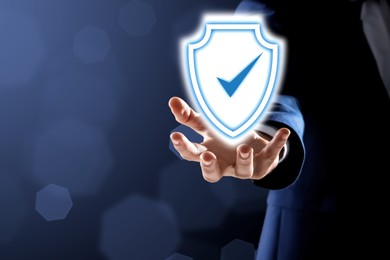 Image of Anti-fraud security system. Man with illustration of checkmark in shield on dark background, closeup. Space for text