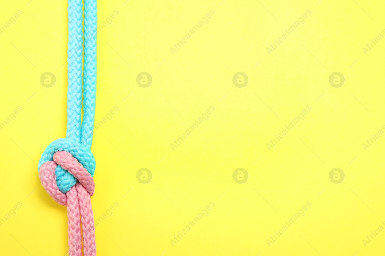 Photo of Top view of colorful ropes tied together on yellow background, space for text. Unity concept