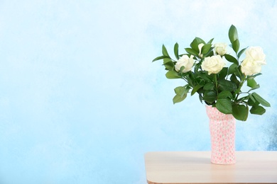 Photo of Vase with bouquet of beautiful roses on table against color background. Space for text