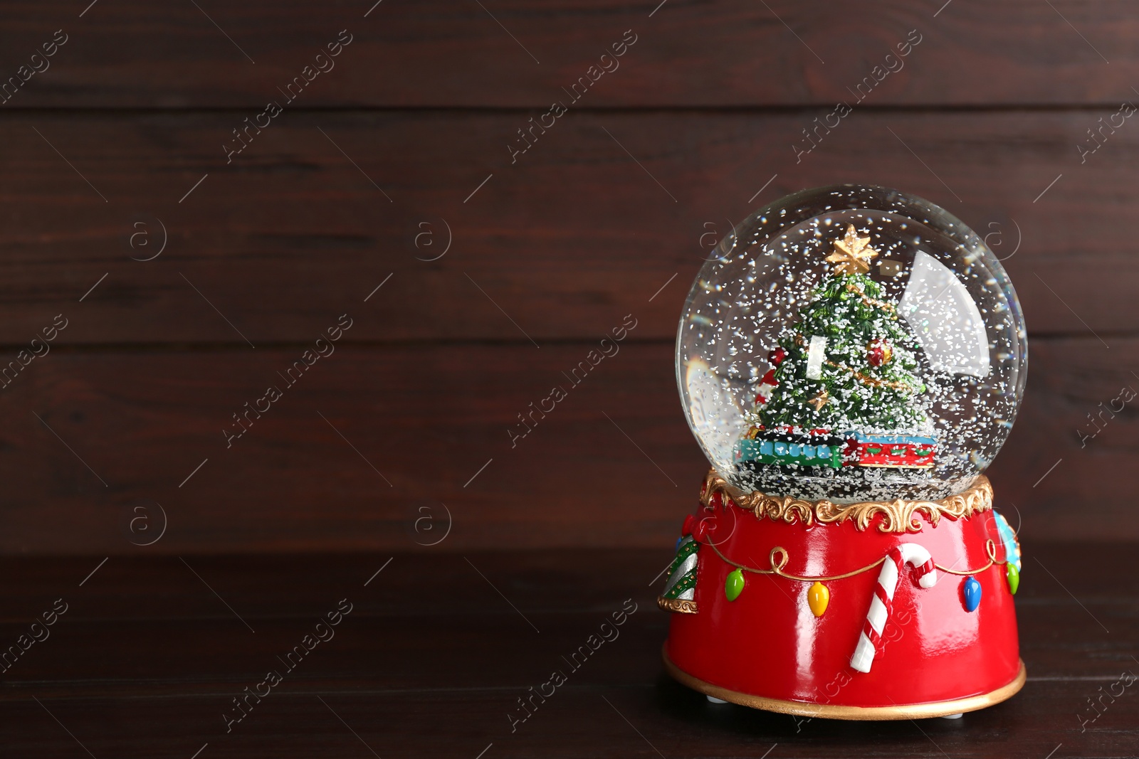 Photo of Beautiful snow globe with Christmas tree on wooden table, space for text