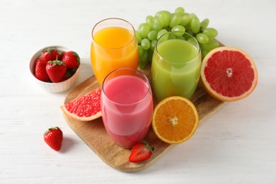 Photo of Wooden board with different juices and fresh fruits on table