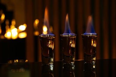 Photo of Flaming alcohol drink in shot glasses on mirror surface against blurred background