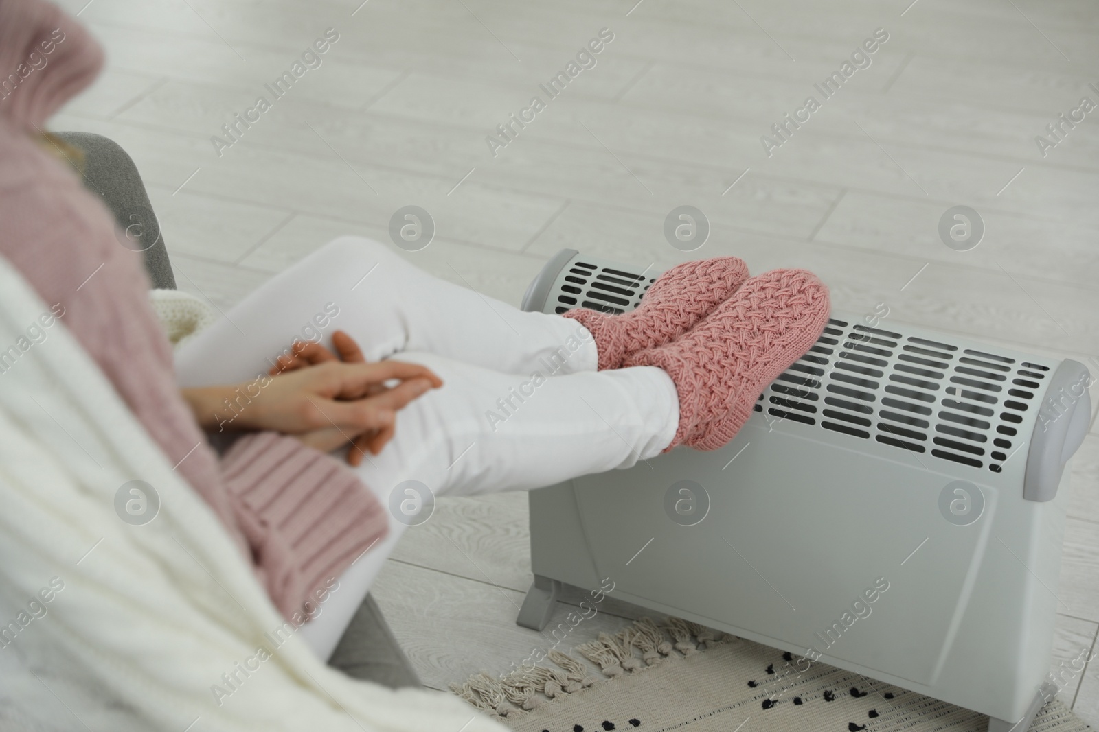 Photo of Woman warming feet on electric heater at home, closeup