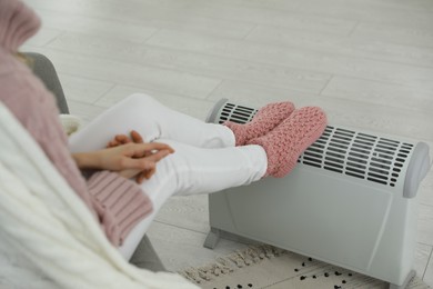 Woman warming feet on electric heater at home, closeup