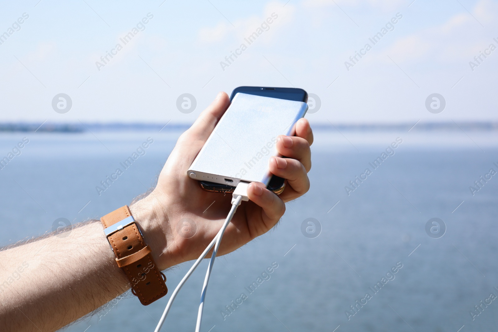 Photo of Man charging mobile phone with power bank near river, closeup