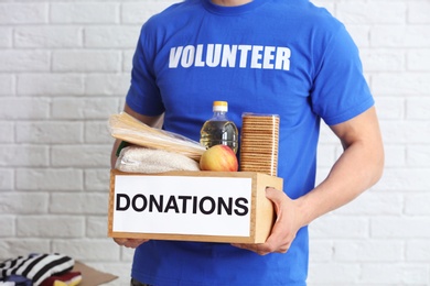 Photo of Male volunteer holding donation box with food products indoors