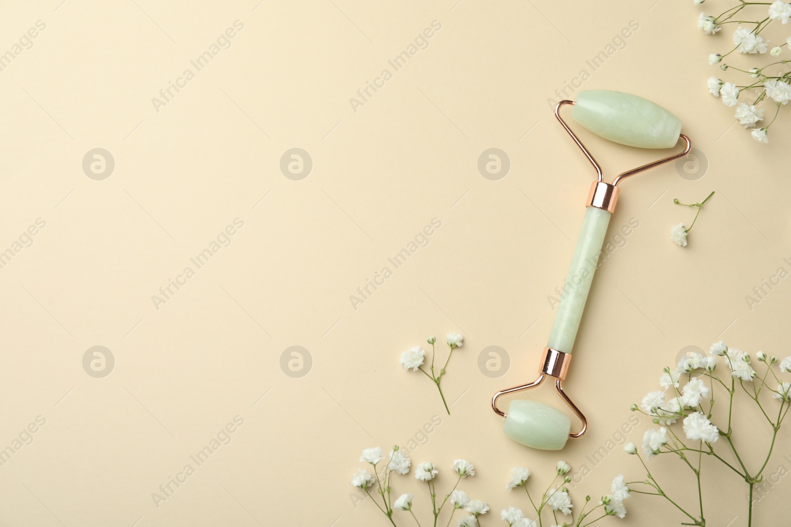 Photo of Natural face roller and flowers on beige background, flat lay. Space for text