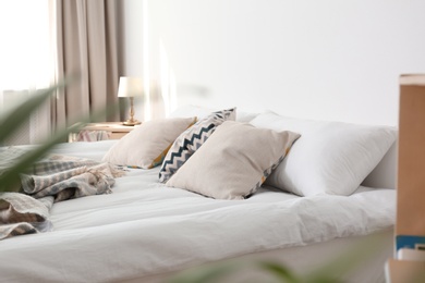 Bed with pillows and plaid near light wall. Cozy interior design