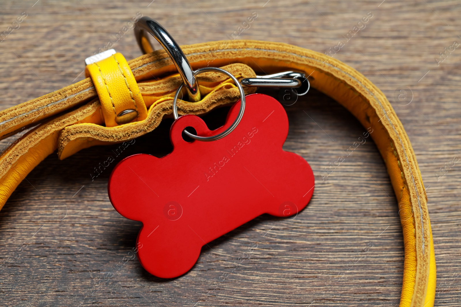 Photo of Yellow leather dog collar with red tag in shape of bone on wooden table, closeup. Space for text