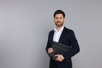 Photo of Happy real estate agent with leather portfolio on grey background. Space for text