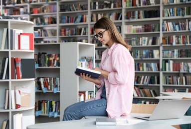 Photo of Young beautiful woman with book in library