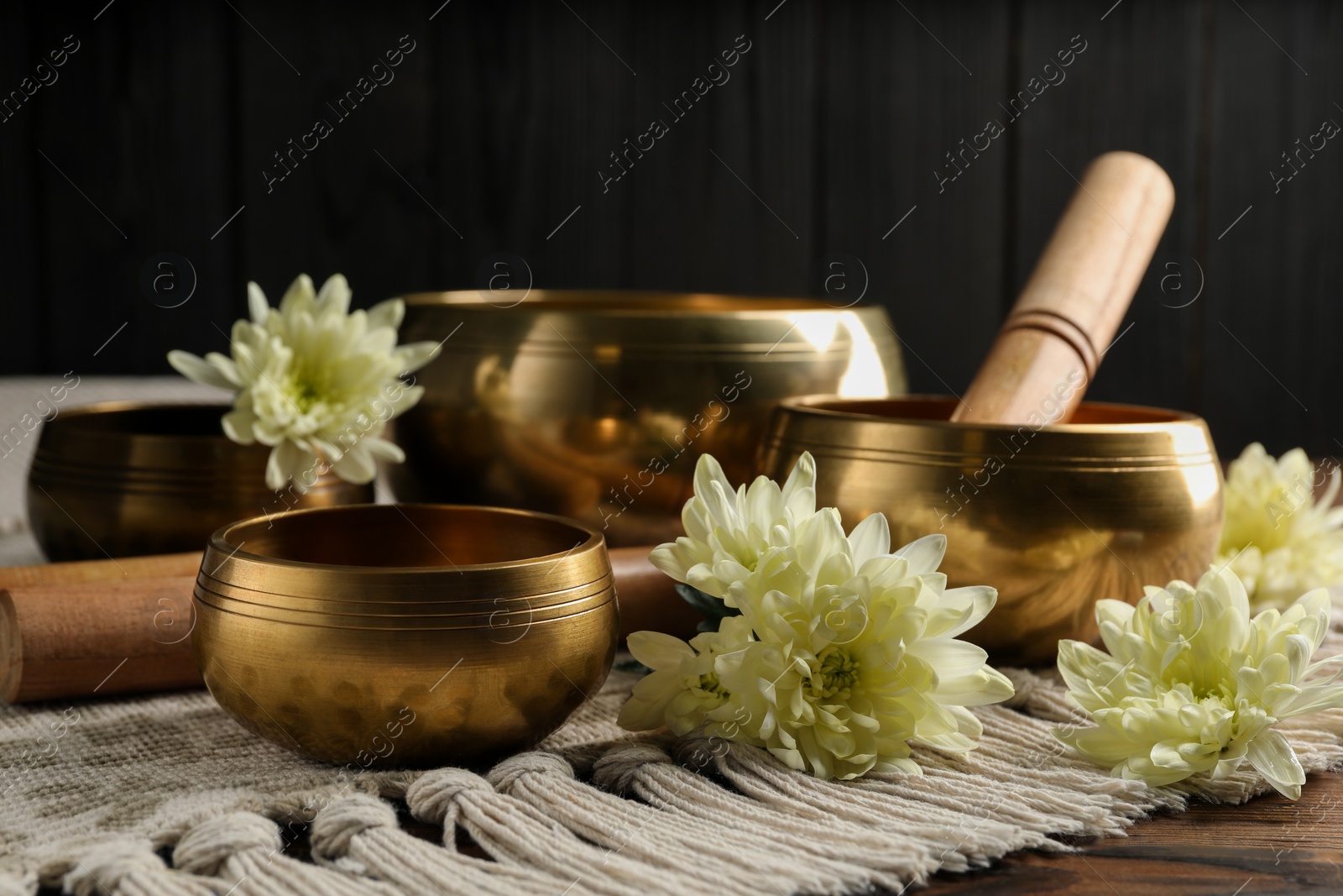 Photo of Tibetan singing bowls with beautiful flowers and mallet on wooden table