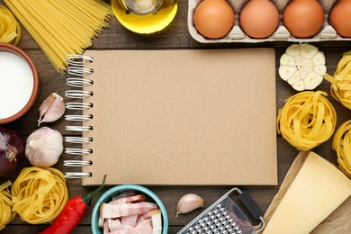 Blank recipe book surrounded by different ingredients on wooden table, flat lay. Space for text