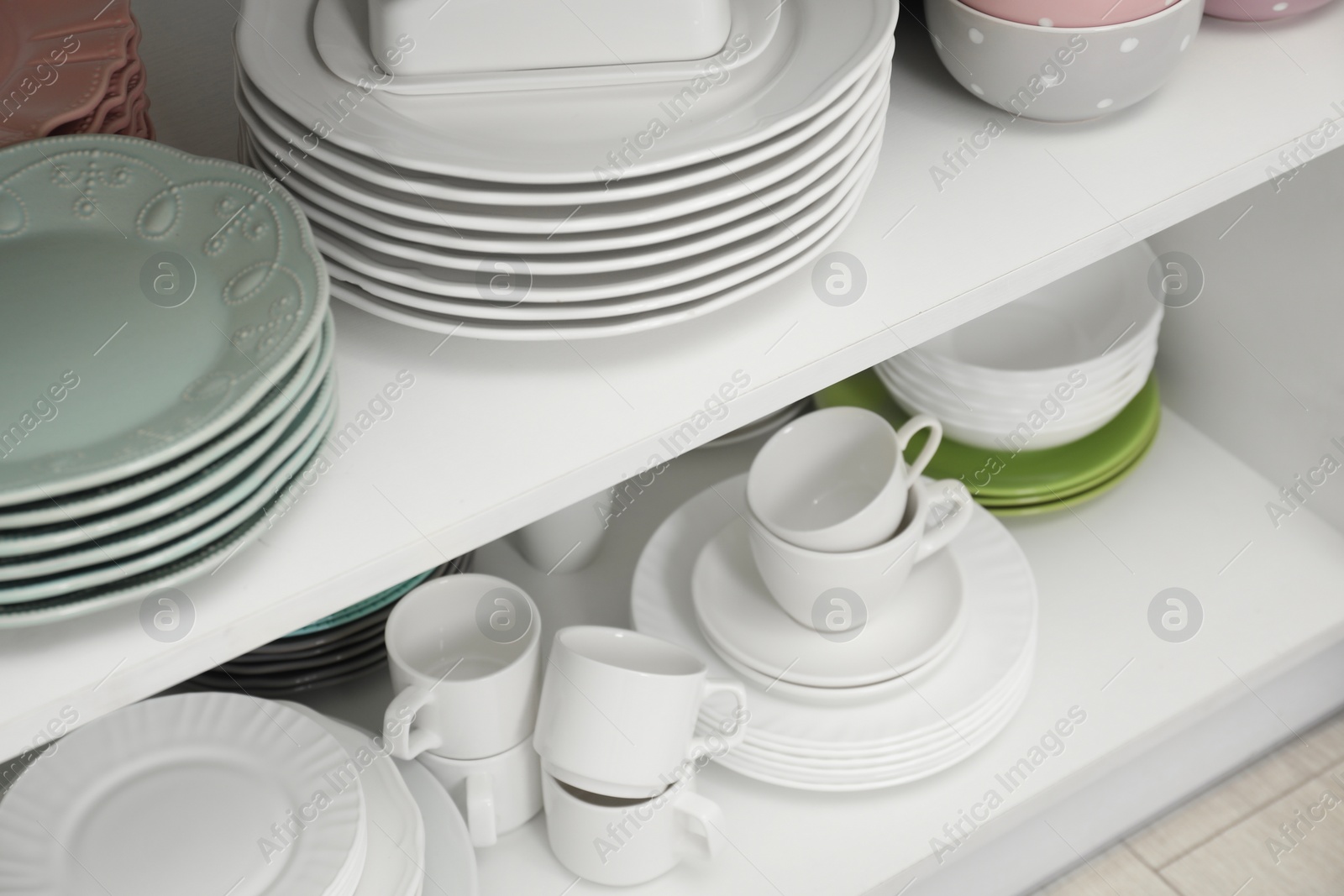 Photo of Clean plates, bowls and cups on shelves in cabinet indoors