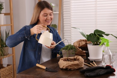 Photo of Woman watering houseplants after transplanting at wooden table indoors