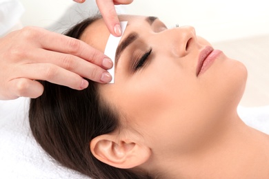 Photo of Young woman having professional eyebrow correction procedure in beauty salon