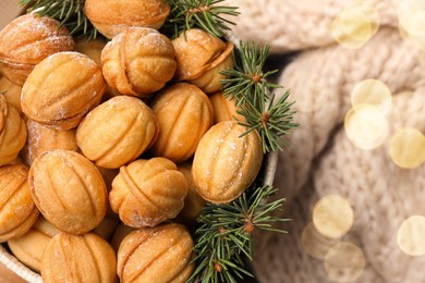 Bowl of delicious nut shaped cookies and fir tree branches on knitted fabric, flat lay