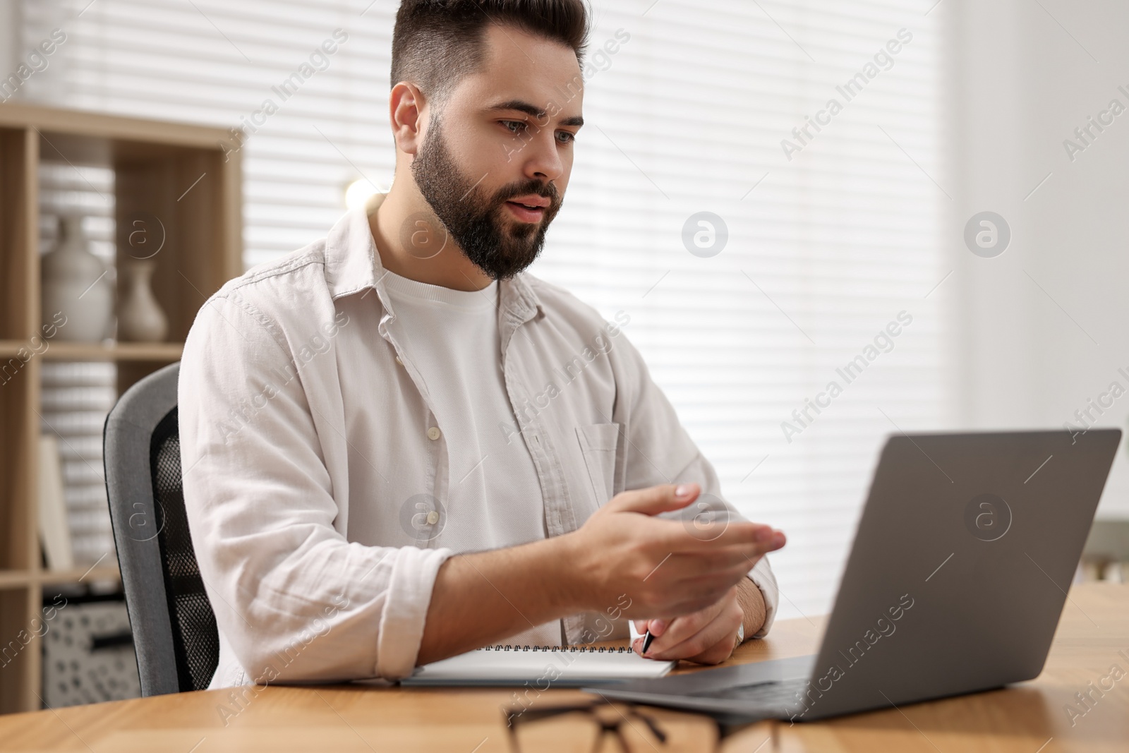 Photo of Young man using video chat during webinar at table in room