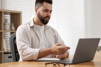 Young man using video chat during webinar at table in room