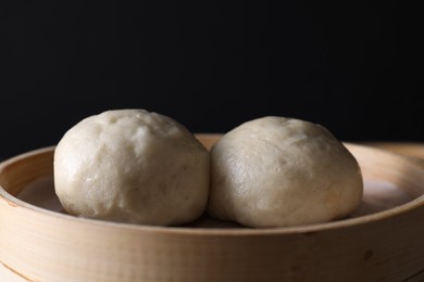 Photo of Delicious Chinese steamed buns in bamboo steamer against black background, closeup