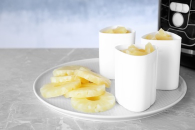 Photo of Tray with cups of yogurt and pineapple slices on table against color background. Multi cooker recipe