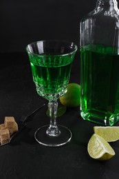 Absinthe, spoon, brown sugar and lime on black table. Alcoholic drink