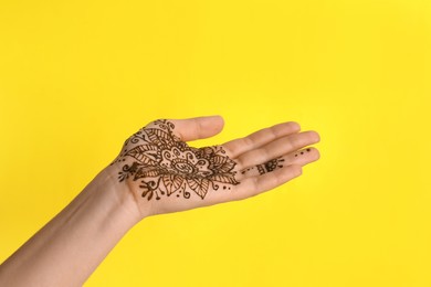Woman with henna tattoo on palm against yellow background, closeup. Traditional mehndi ornament