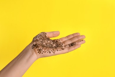 Photo of Woman with henna tattoo on palm against yellow background, closeup. Traditional mehndi ornament