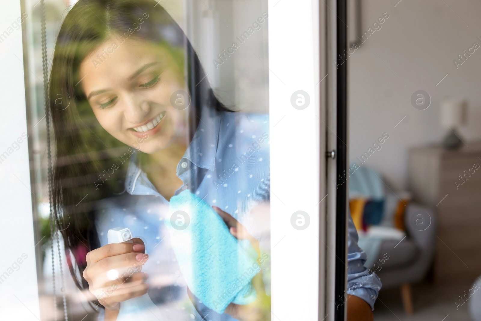 Photo of Young woman cleaning window glass at home