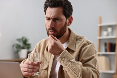 Photo of Worried man with glass of water taking pill from headache at workplace