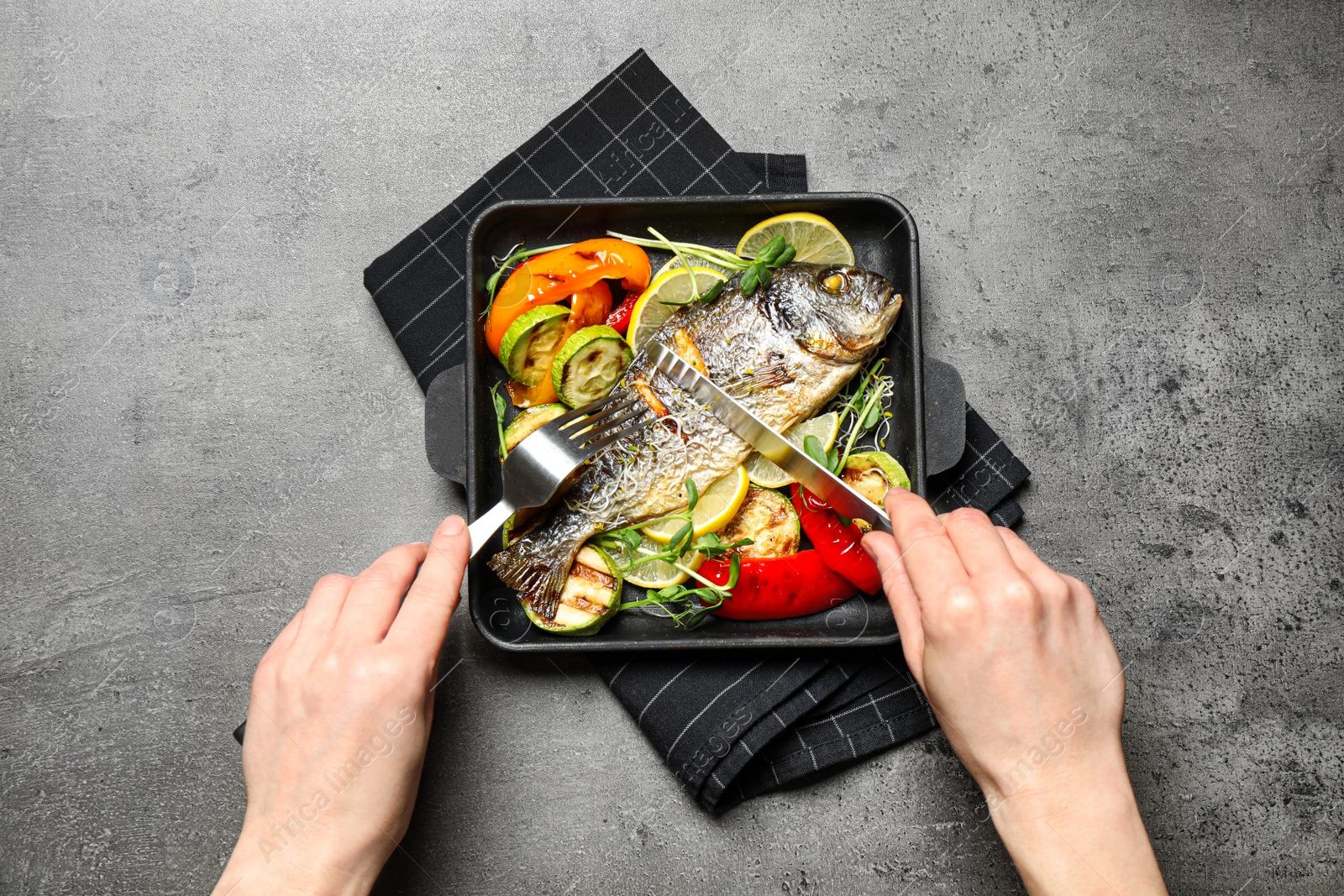 Photo of Woman eating delicious roasted fish at grey table, top view